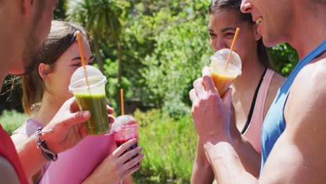 happy diverse group of men and women making a toast with health drinks after yoga class in park