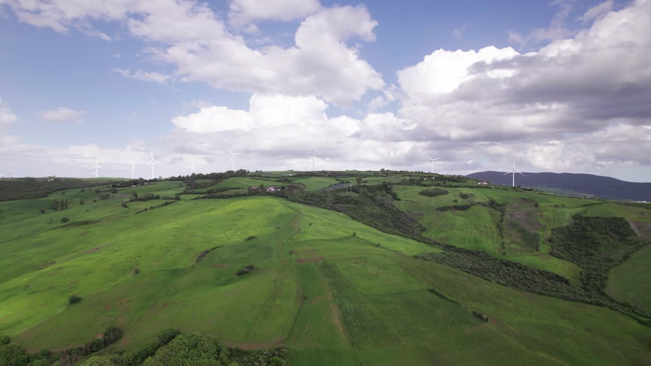 Paesaggio aereo di una turbina eolica in cima a una collina verde all'orizzonte in una giornata di sole con cumuli.