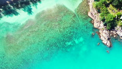 Turquoise-lagoon-with-coral-reefs-on-white-sand-near-rocky-coast-of-tropical-island-with-green-lush-vegetation-in-Myanmar