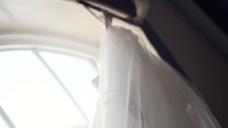 close up to the top of a beautiful wedding dress as it hangs from a large window sill