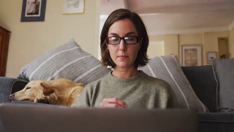 Mujer-Caucásica-Usando-Una-Computadora-Portátil-Trabajando-Desde-Casa-Con-Su-Perro-Junto-A-Ella-En-El-Sofá