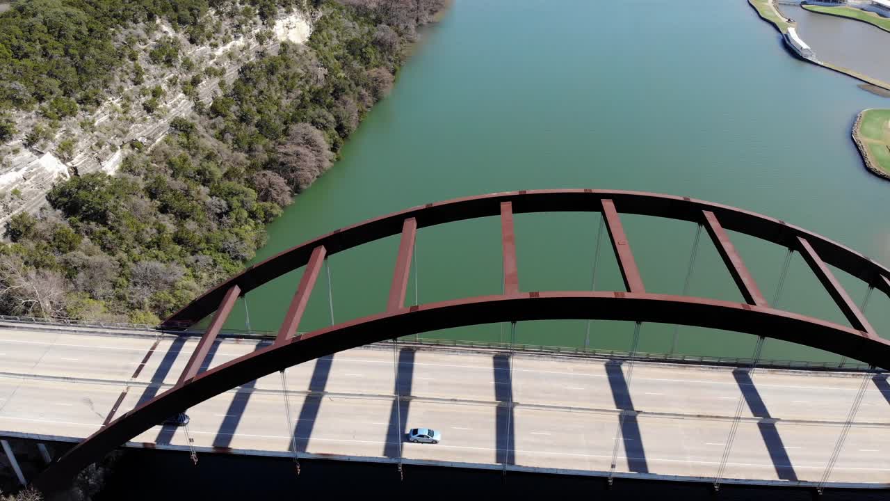 Aerial Austin Pennybacker Bridge - flying towards the bridge which is offset to the right, panning the camera down to reveal top down view just as it cross the bridges deck - continues to other side.