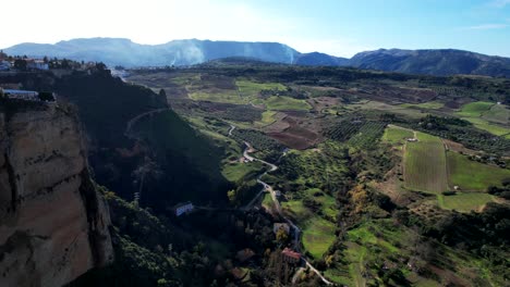 tilt down of cliffside homes casting dramatic shadows over farmland fields below
