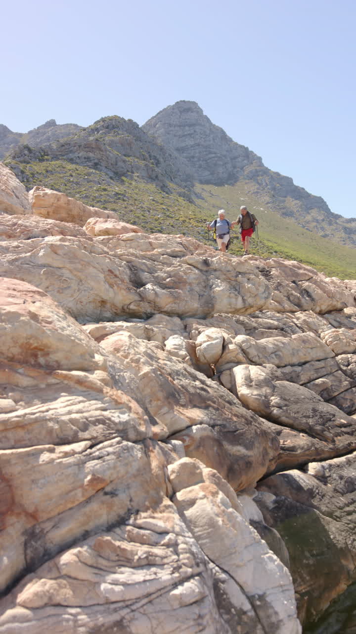Vertical video of senior biracial couple hiking in mountains, in slow motion