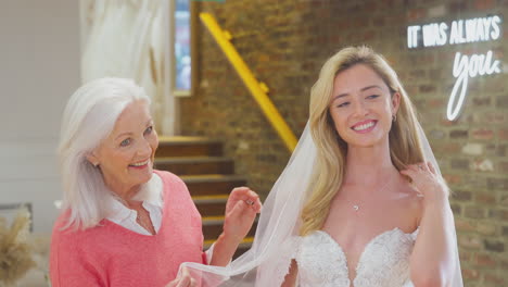 grandmother watching adult daughter choosing and trying on wedding dress in bridal store