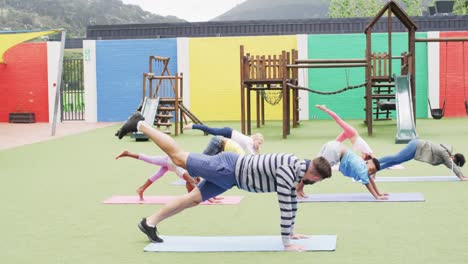 diverse male teacher and happy schoolchildren exercising on mats at school playground