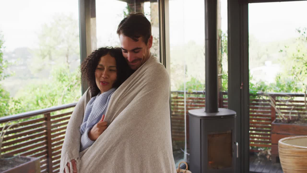 Smiling mixed race couple wrapped in sheets embracing each other in the balcony at vacation home