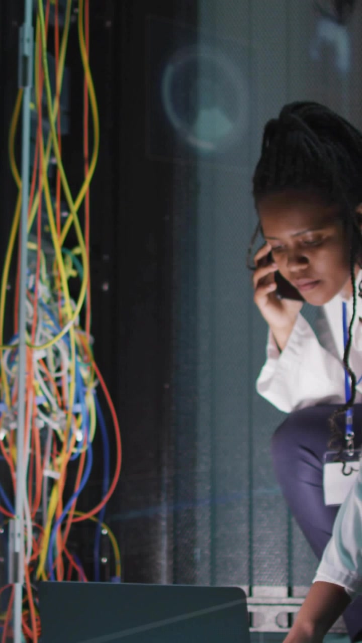 Vertical video: Tech kneeling rack, taking call while testing cables and fixing network via laptop