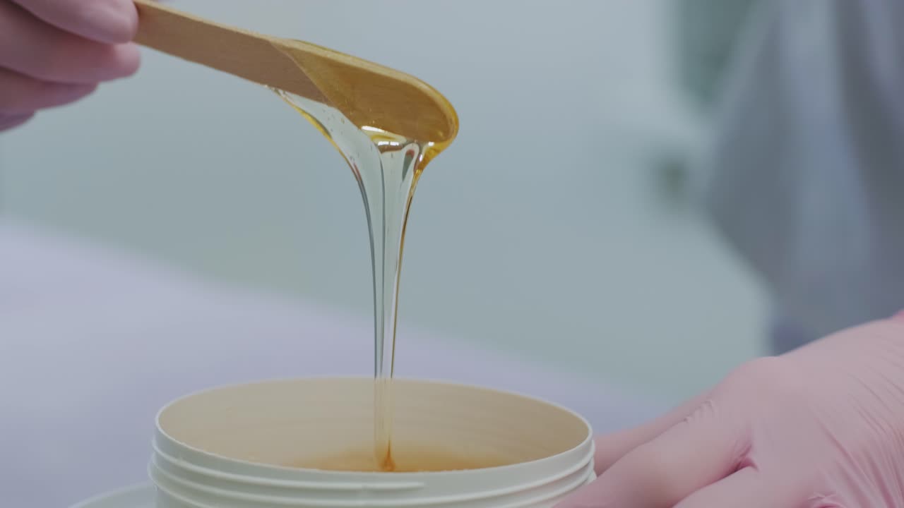 Liquid sugar for skin epilation. Close up shot. depilation and beauty concept - sugar paste or wax honey for hair removing with wooden waxing spatula sticks