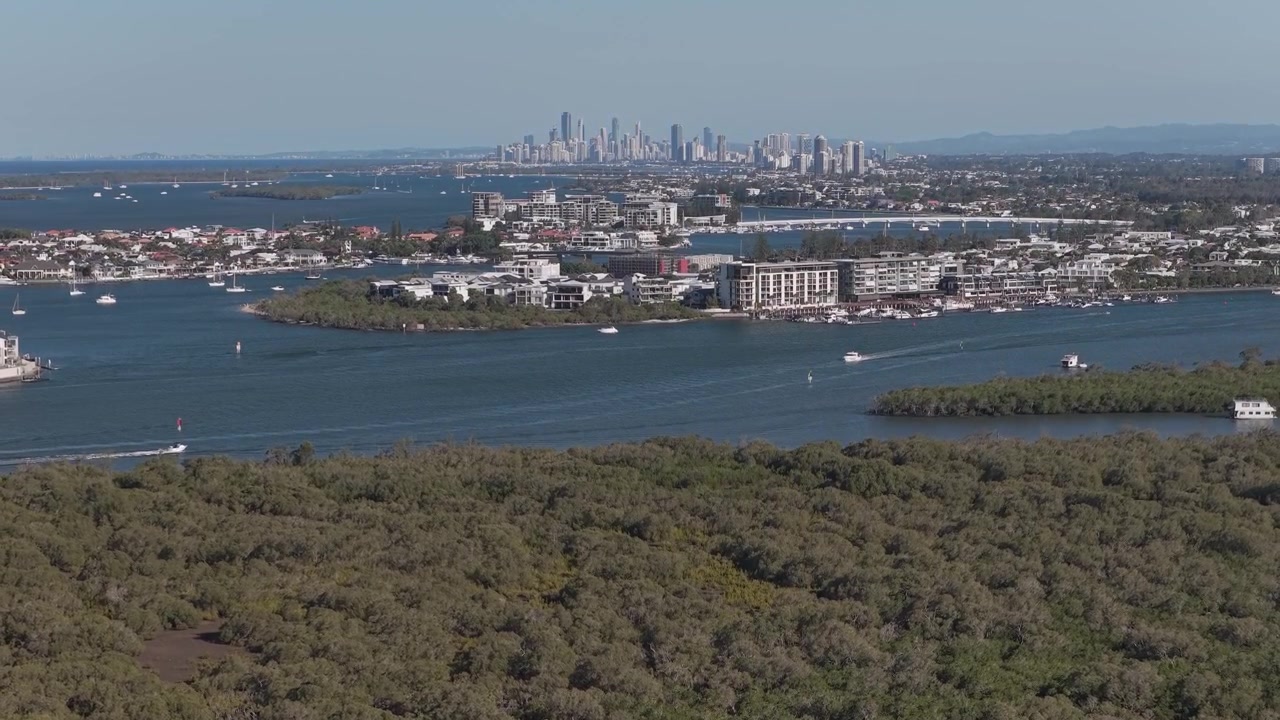 Via navigabile di Gold Coast con barche, appartamenti costieri, dense mangrovie e vista dello skyline di Surfers Paradise in lontananza. Ripresa aerea con allontanamento e ascesa
