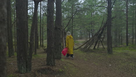 woman in yellow raincoat with red bag walking along through forest toward sea, captured with a steady camera