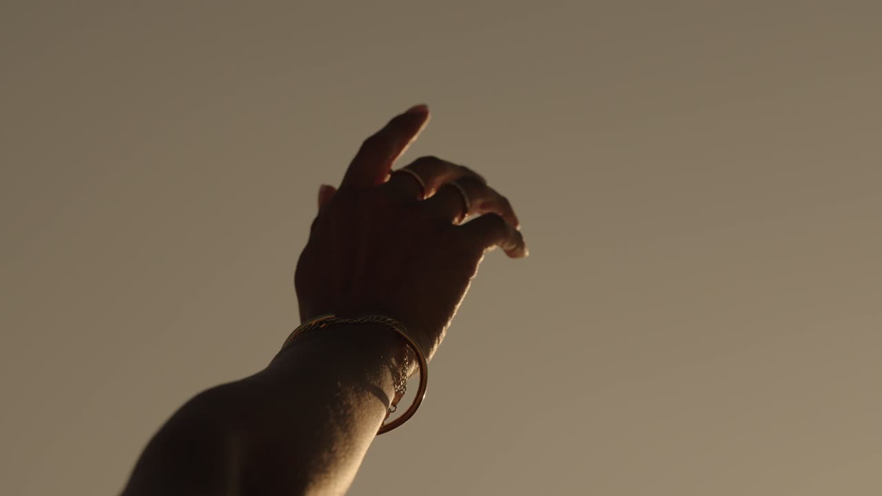 A woman's hand adorned with rings and a bracelet reaches gracefully into warm light on the coast of Portugal