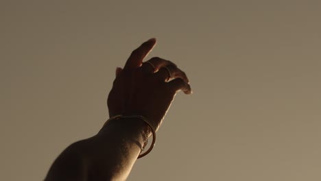a woman's hand adorned with rings and a bracelet reaches gracefully into warm light on the coast of portugal