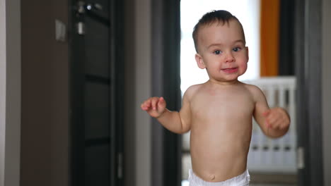 smiling caucasian baby in diaper running up to camera. lovely kid being active at home.