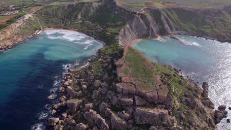 enorme formación rocosa en una playa en malta con agua azul a ambos lados, vista desde un dron