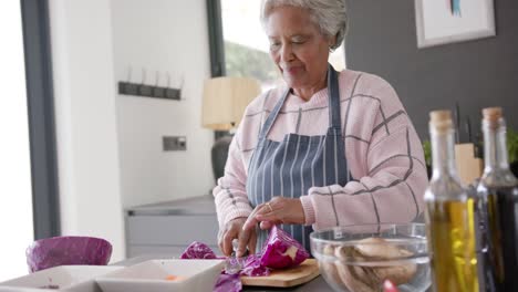 senior biracial woman cooking dinner and chopping vegetables in kitchen, unaltered, in slow motion