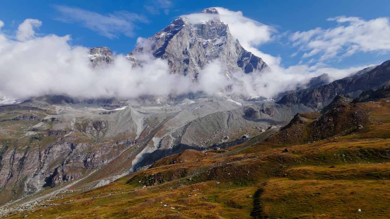 Push in aerial establishing shot showing golden vegetation leading to a tall snow covered mountain in Cervinia, Italy, capturing dramatic alpine contrast and scenery