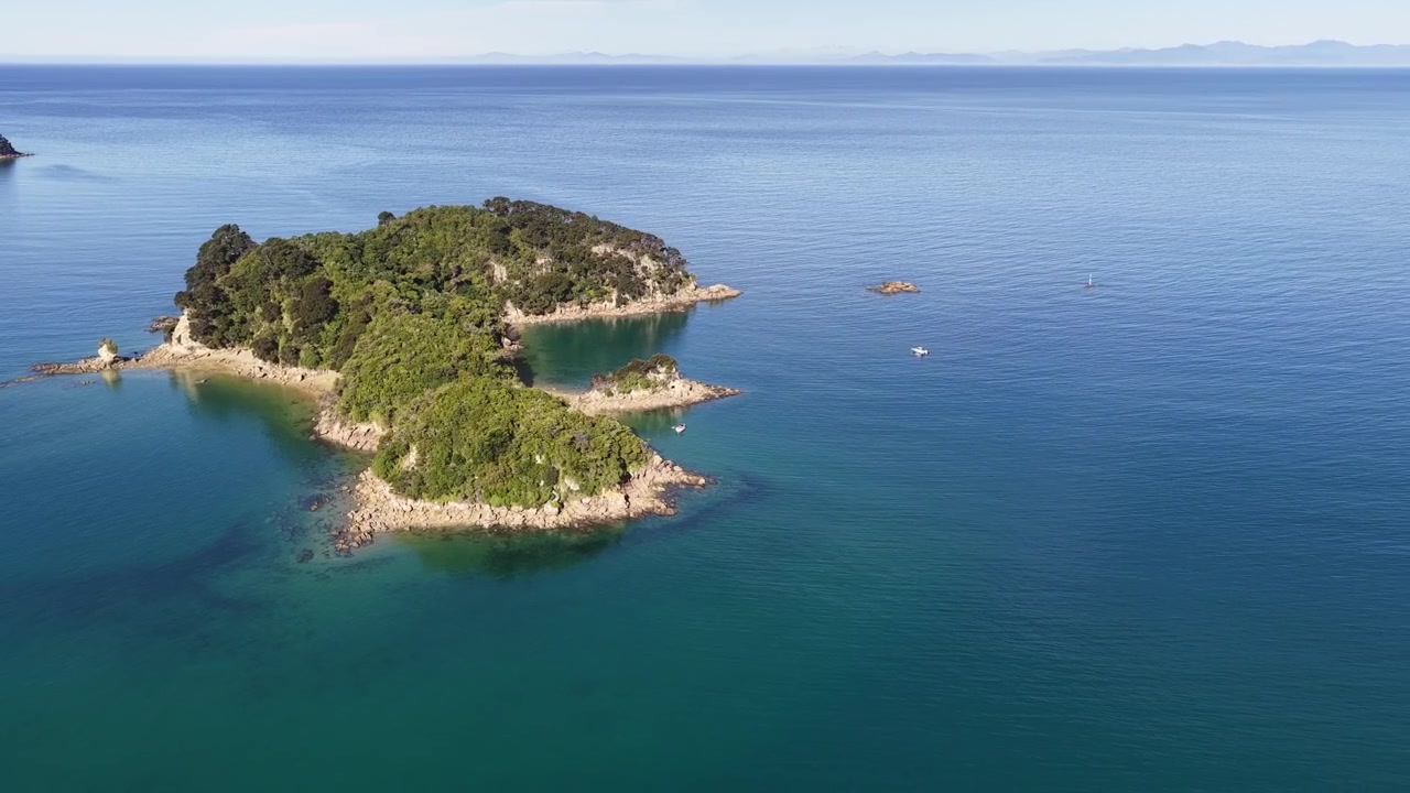 Ripresa cinematografica con drone in allontanamento che rivela un'isola appartata circondata da un oceano blu calmo in Nuova Zelanda