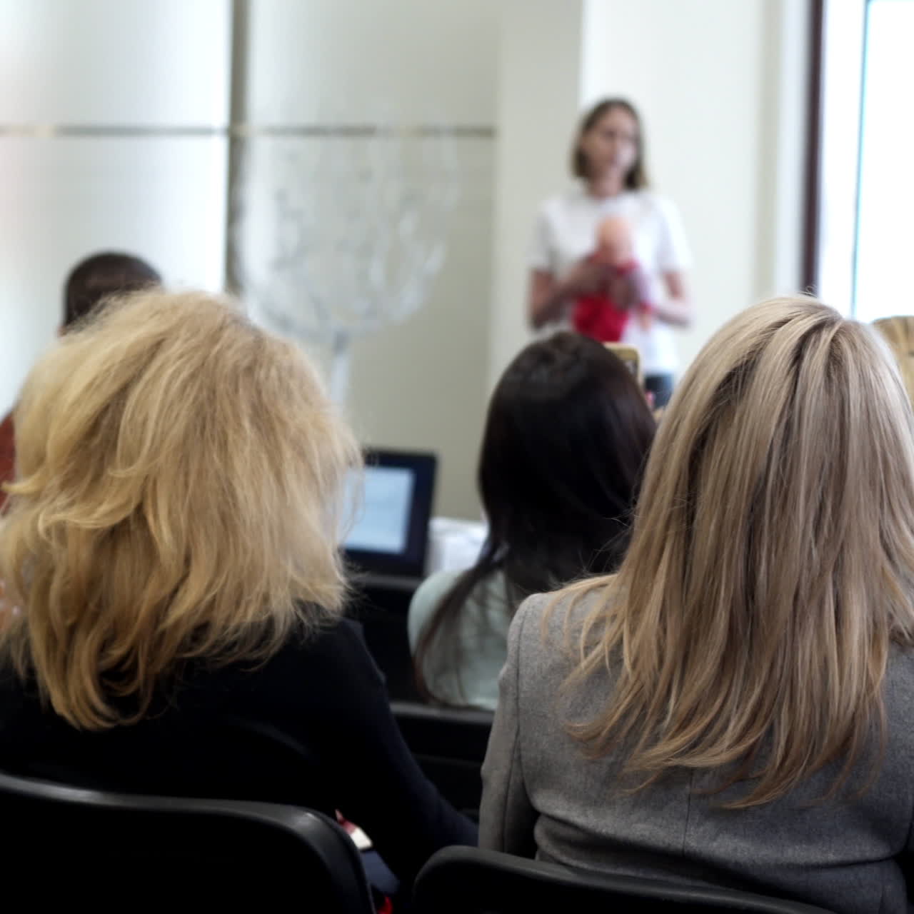 Public audience listening presentation. Female listeners sitting in the auditorium. Woman coach speaker tells speech at conference.