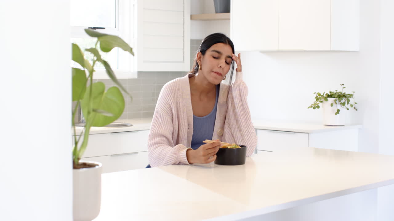 Indian woman enjoying meal with chopsticks in modern kitchen, looking content
