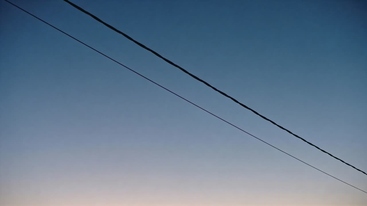 Imagem gravada por câmera portátil, movendo-se sobre o céu da rua, mostrando dois cabos de eletricidade diagonais ao amanhecer.