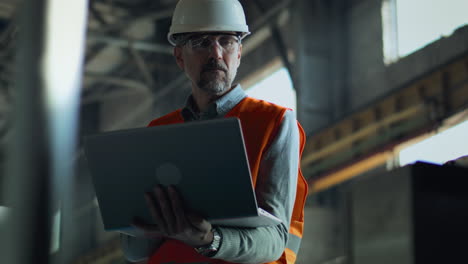 worker inspecting equipment with laptop in factory