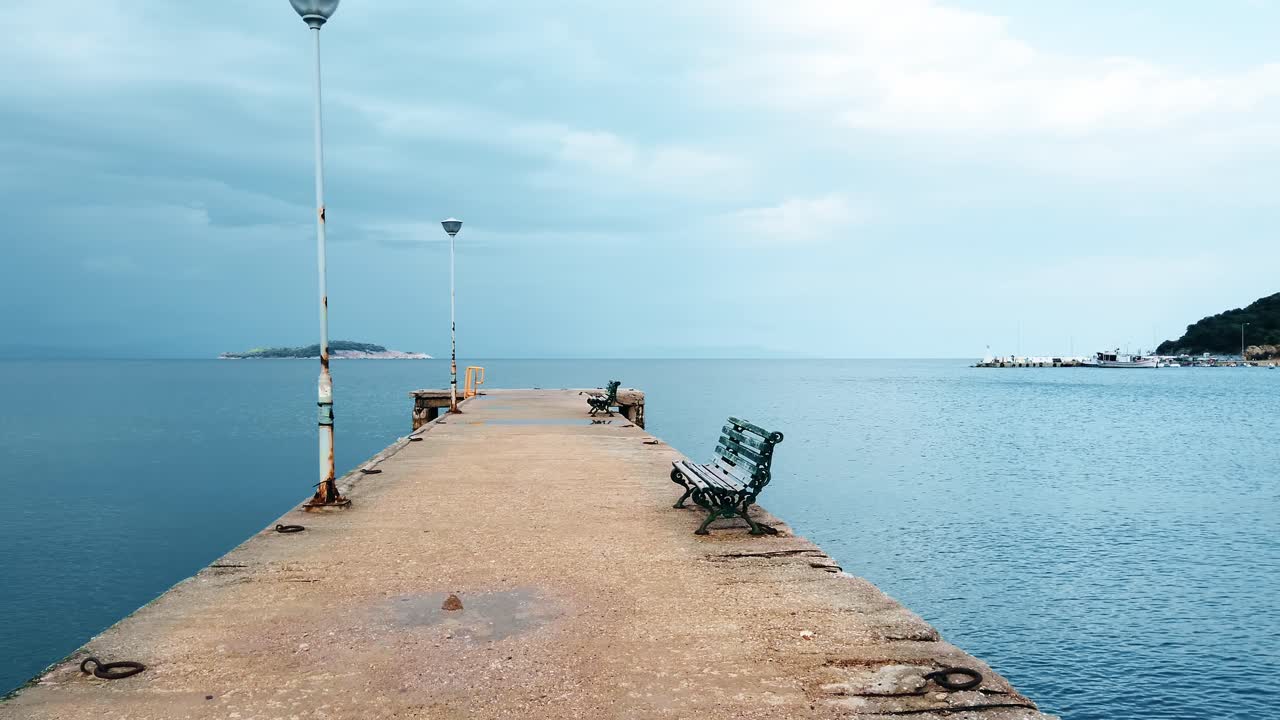 Pier with lamp posts, benches near the Aegean sea coast in Stavros, hills on the background, Greece