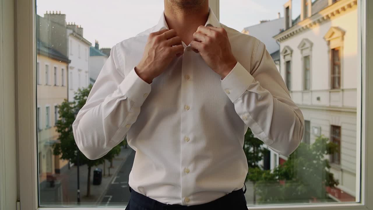 Uomo che si sistema in camicia bianca, che abbottona a casa vicino alla finestra, preparandosi per un incontro