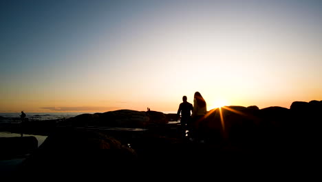 Couple-walks-into-frame-through-sunburst-to-go-watch-sunset-over-ocean