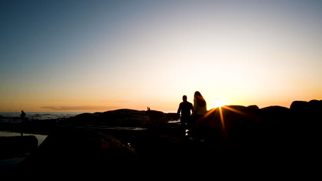 pareja entra en el marco a través de rayos de sol para ir a ver la puesta de sol sobre el océano