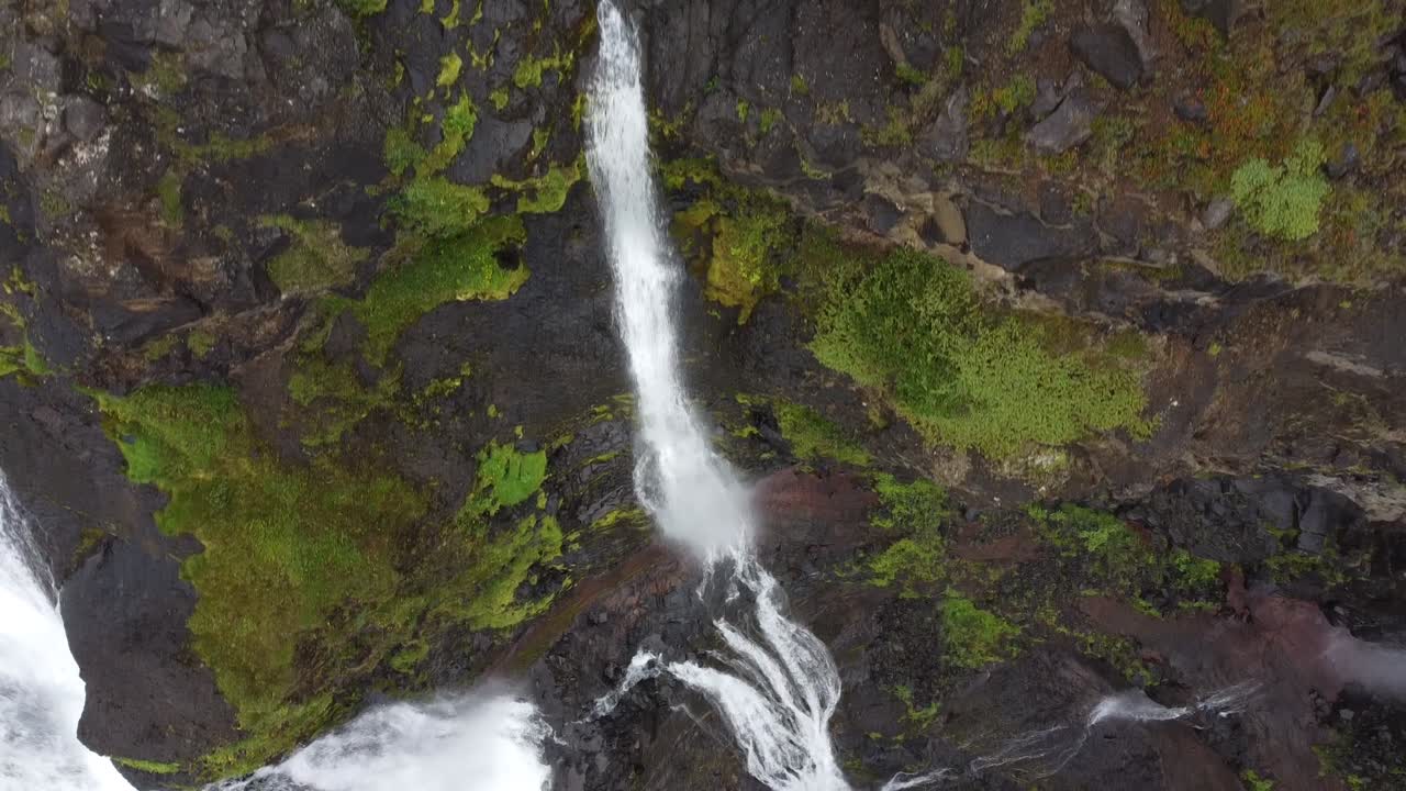 toma aérea inclinada hacia arriba de poderosas cascadas entre montañas rocosas y cubiertas de musgo en el paisaje islandés