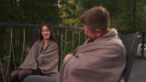 couple wrapped in a blanket, sitting on a deck in the forest