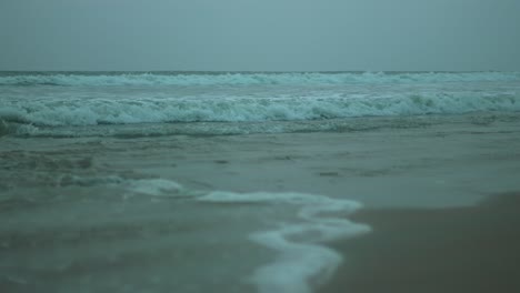 moody waves crashing on a sandy beach under overcast skies, calm yet powerful