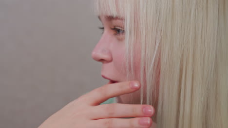 close up of young blonde girl licking finger, soft natural lighting highlighting facial features and hand, casual moment showing simple action, indoors setting with neutral background