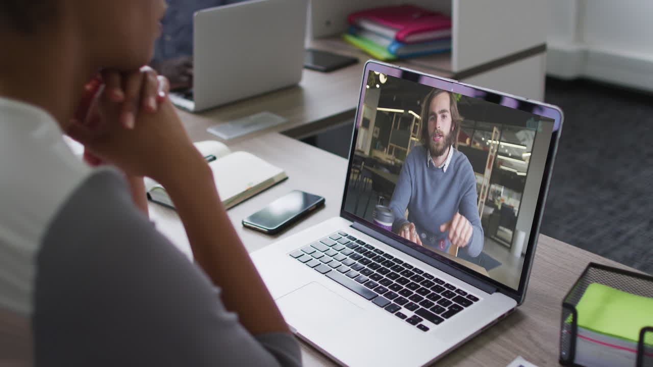 African american businesswoman sitting at desk using laptop having video call with male colleague