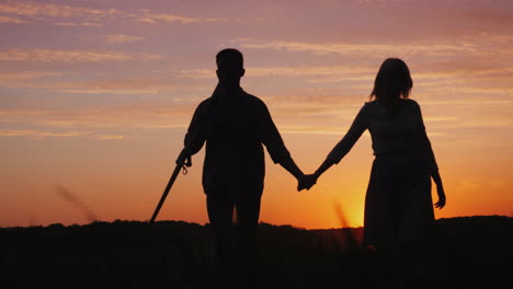 a young couple of farmers walking across the field to meet the camera silhouettes at sunset 4k video