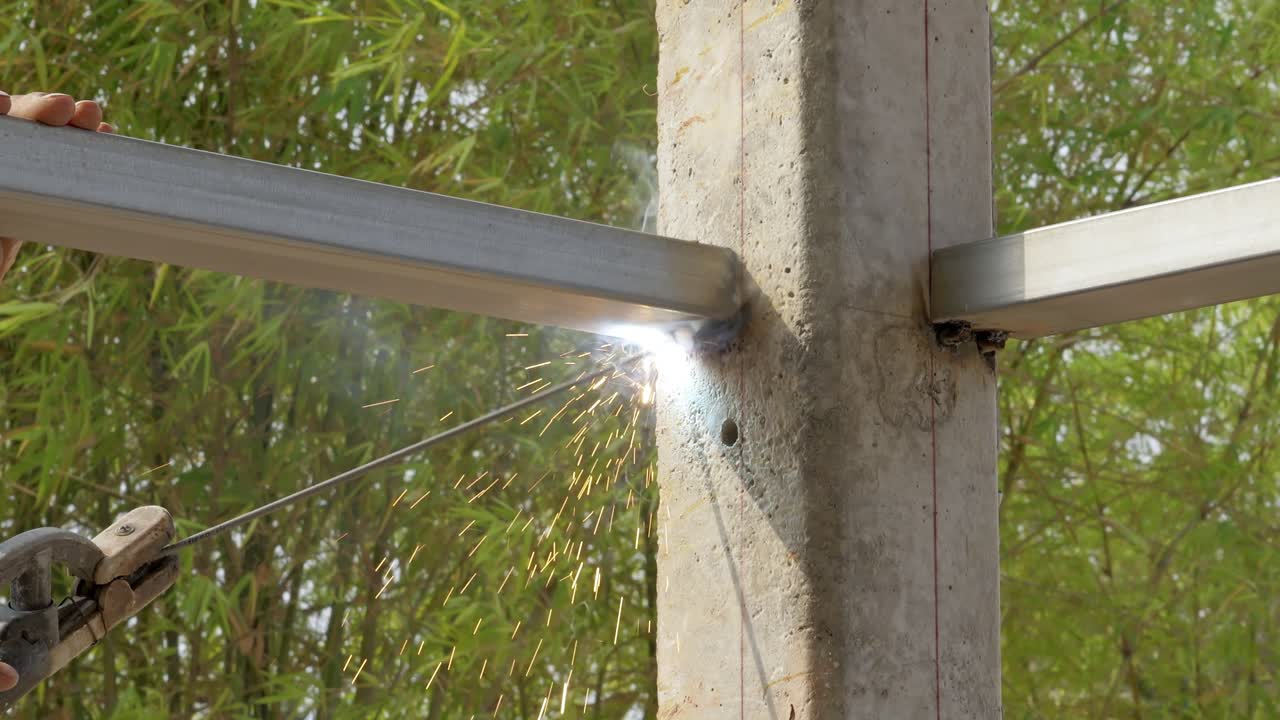 Un saldatore che fonde travi metalliche in un cantiere edile, mostrando l'attività industriale immersa nella natura.