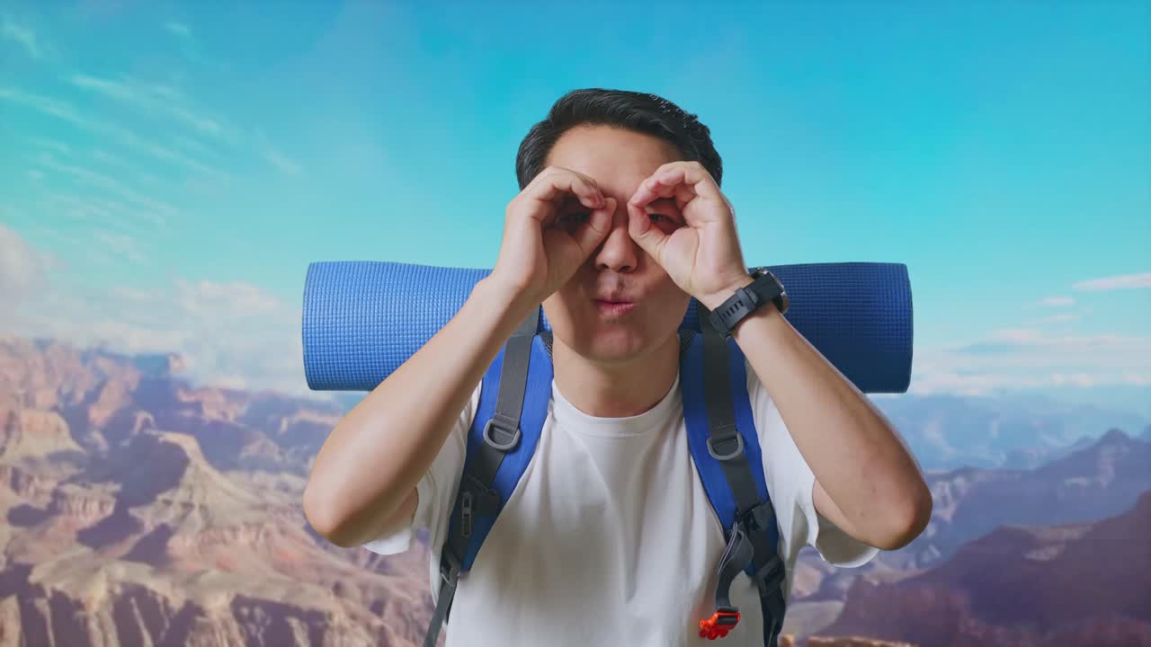 Close Up Of Asian Male Hiker With Mountaineering Backpack Smiling And Making Binoculars Gesture Then Looking Around While Traveling At The Top Of Mountain
