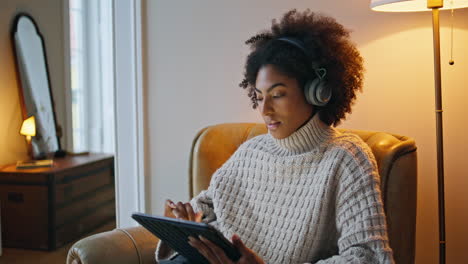 Relaxed-model-watching-tab-at-lamp-light-place.-African-woman-sitting-armchair