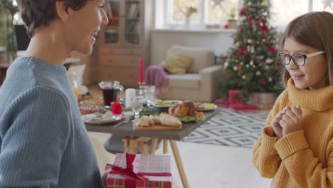 Brünette-Kurze-Haare-Mutter-Gibt-Ihrer-Tochter-Ein-Weihnachtsgeschenk-Im-Wohnzimmer-Mit-Weihnachtsschmuck