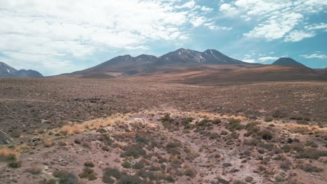 Drone-flying-near-the-dry-ground-of-the-Chilean-desert-with-a-volcano-on-the-background