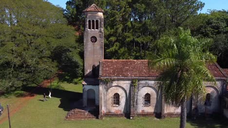 Drohnenübergang-Der-Alten-Kirche-Mit-Roten-Fliesen-Und-Turm-In-Santa-Inés,-2-Personen-Gehen-Weg