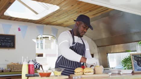 portrait of african american man wearing apron smiling while preparing burgers in the food truck