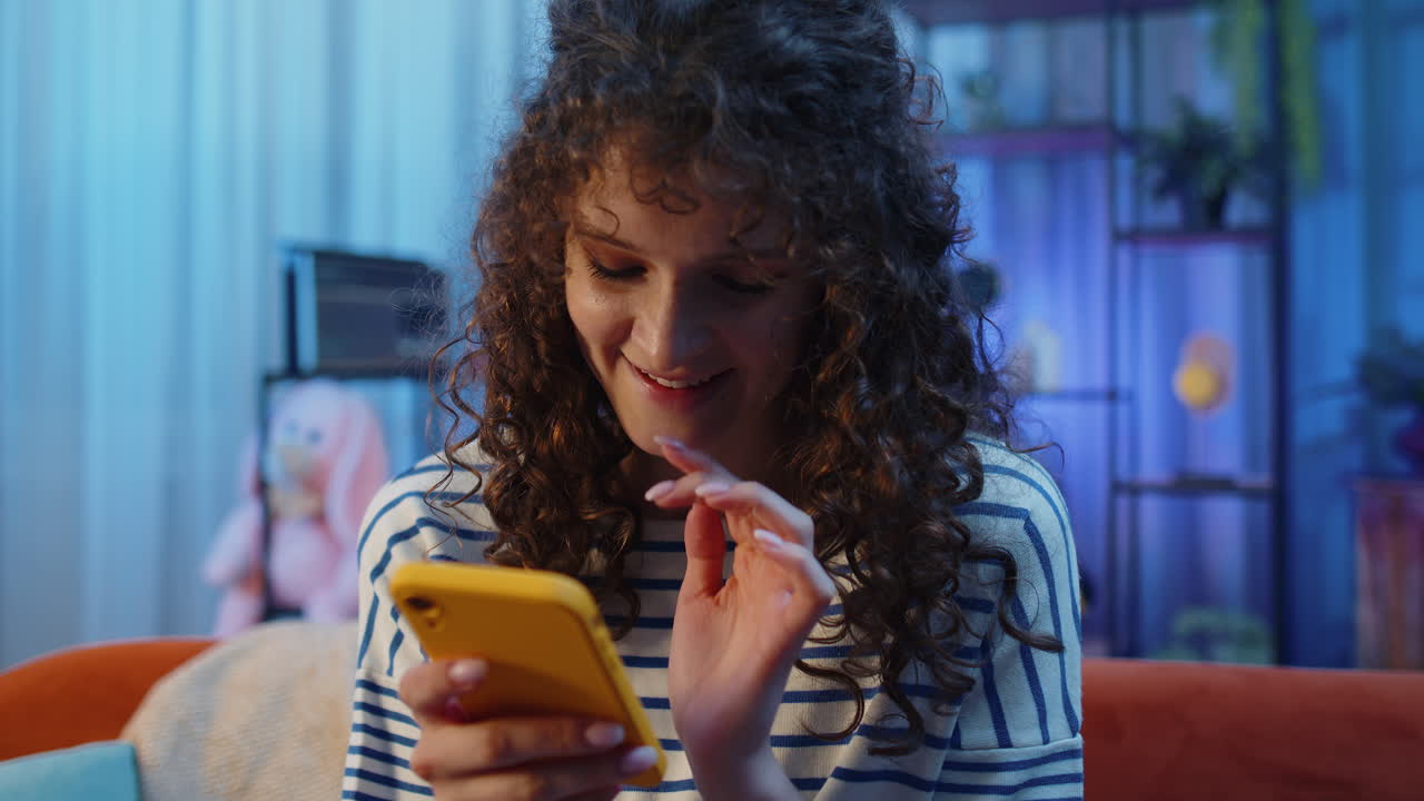 joven mujer morena sentada en el sofá, usando un teléfono inteligente para compartir mensajes en la aplicación de redes sociales