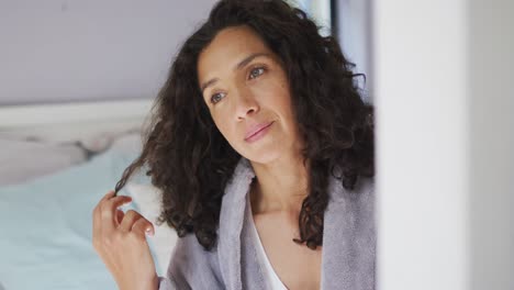 happy mixed race woman wearing pajamas and playing with hair in bedroom