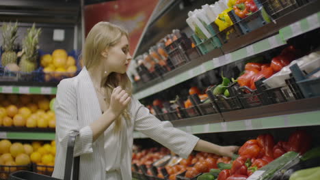 The-girl-housewife-shopping-at-the-supermarket.-Chooses-fresh-tomatoes-on-a-branch-puts-them-in-a-cellophane-bag-ties.-Them-and-puts-them-into-a-cart.