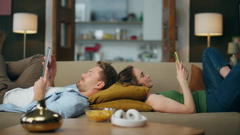 Pareja-Relajada-Navegando-Por-El-Sofá-De-Los-Gadgets.-Mujer-Mensajes-De-Texto-Teléfono-Chico-Leyendo