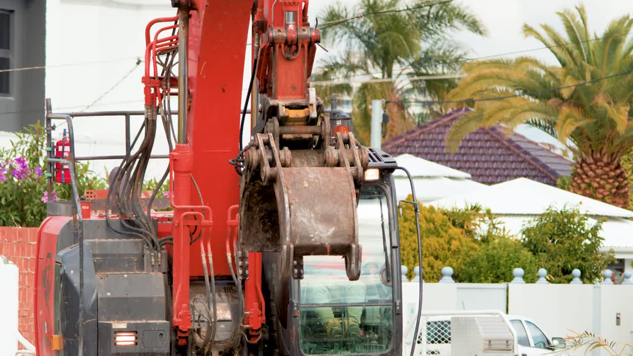 Visão detalhada do braço de uma escavadeira vermelha e da cabine do operador durante o trabalho de limpeza em um terreno residencial