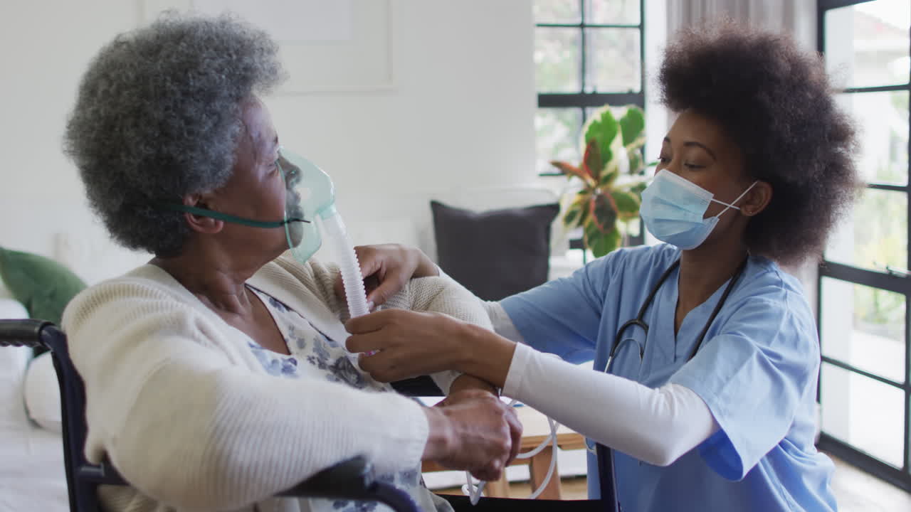 African american female doctor giving oxygen to senior female patient in wheelchair, slow motion