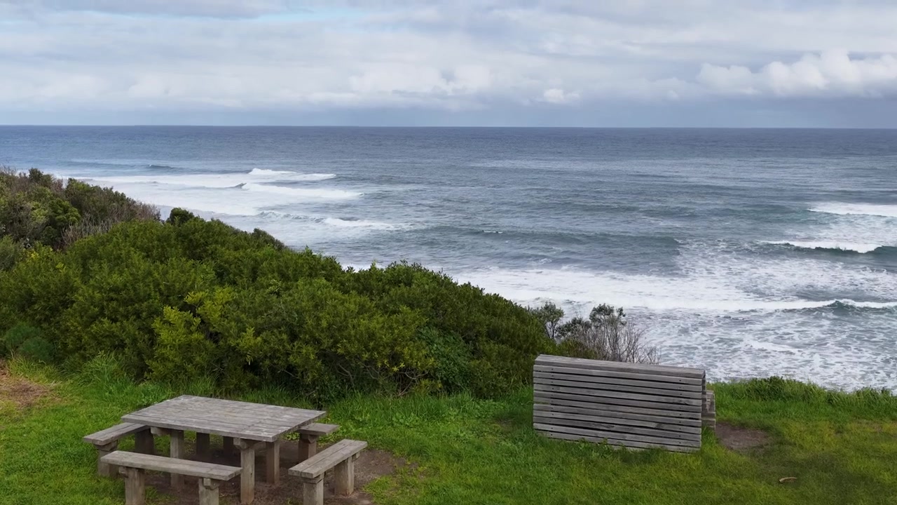 Vidvinkelbillede af rullende brænding og blåt vand under overskyet himmel i Mornington Peninsula, Australien.